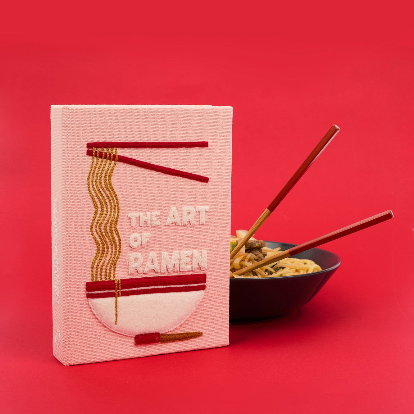 Clutch titled 'The Art of Ramen' with a bowl of ramen and chopsticks on a red background